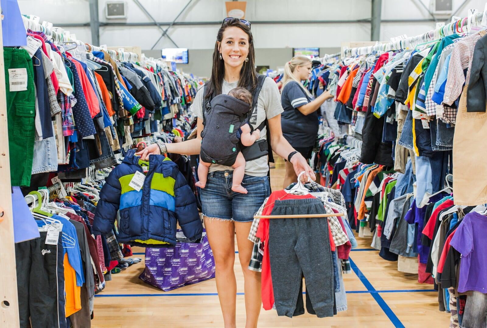 A young JBF shopper mom in a black Metallica T-shirt holds an outfit she intends to buy at her local JBF sale.